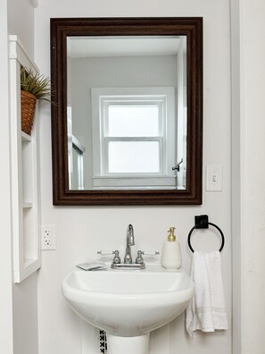 A bathroom with a white sink, a mirror with a dark frame, a towel ring, and a potted plant.