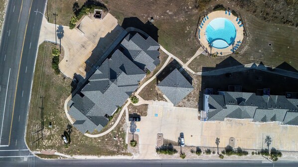 An aerial view of a residential area with a swimming pool, multiple houses, and a road.