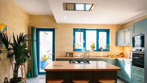 A modern kitchen with a central island, bar stools, and a view to the outside. - Chic Nadur Townhouse with Private Pool & BBQ (In-Nadur)