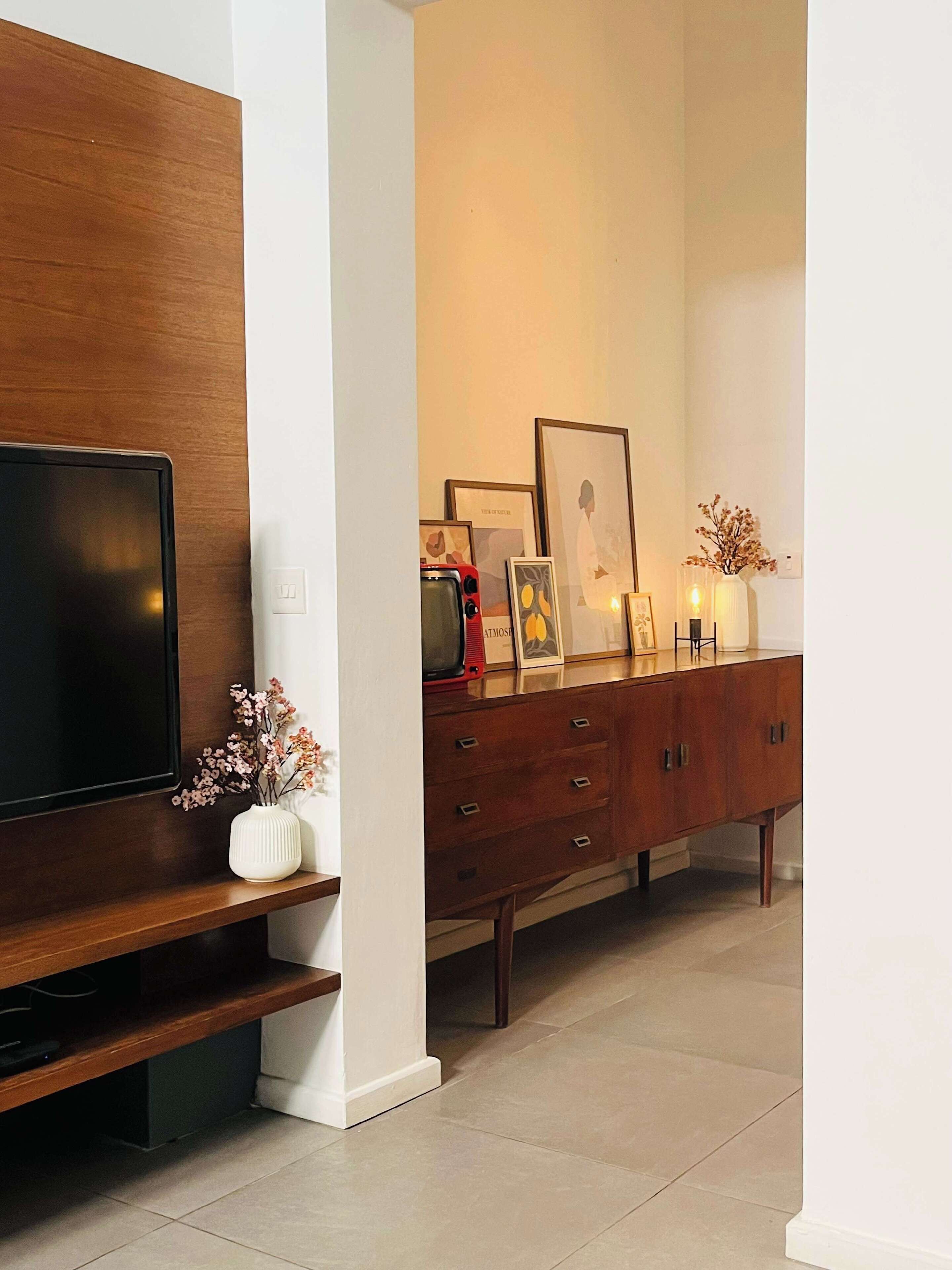 Un salon moderne avec un téléviseur à écran plat fixé à un mur en bois, un meuble en bois doté de tiroirs et un vase blanc contenant des fleurs séchées, posé sur une console.