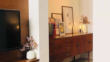 Un salon moderne avec un téléviseur à écran plat fixé à un mur en bois, un meuble en bois doté de tiroirs et un vase blanc contenant des fleurs séchées, posé sur une console.
