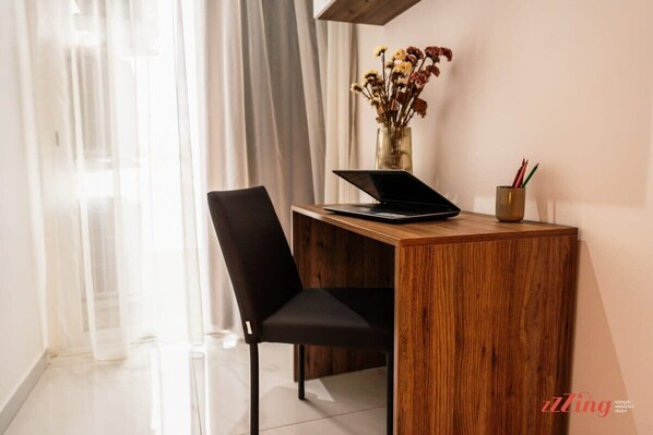 A wooden desk with a laptop, a vase with dried flowers, and a cup with pencils.