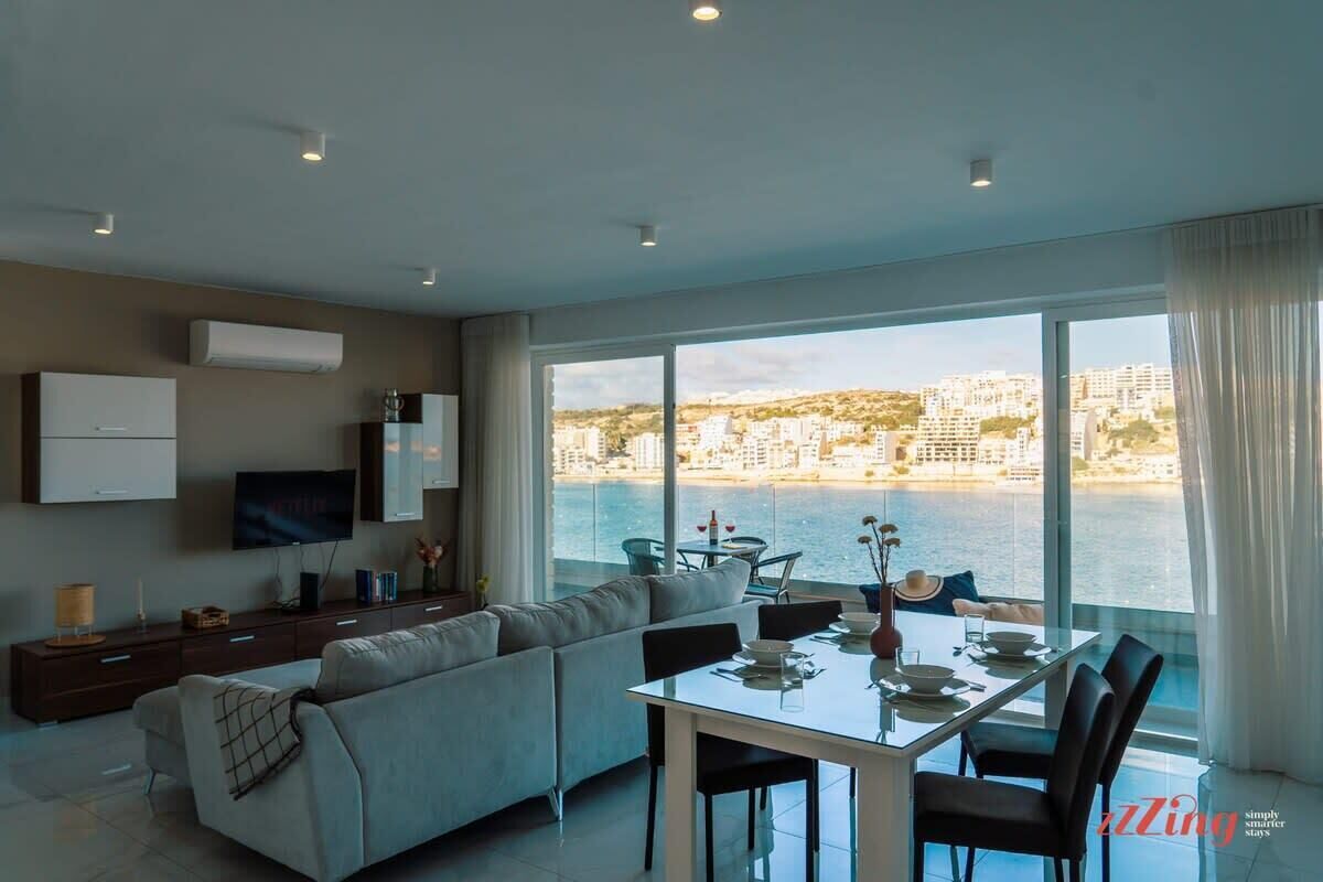 A modern living room with a large window, a dining area, and a sofa.