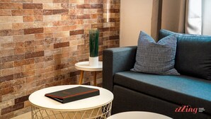 A modern living room with a brick wall, a grey sofa, and a small white table with a book. - Stylish 2BR Duplex Holiday Retreat in St. Paul's (San Pawl il-Bahar)