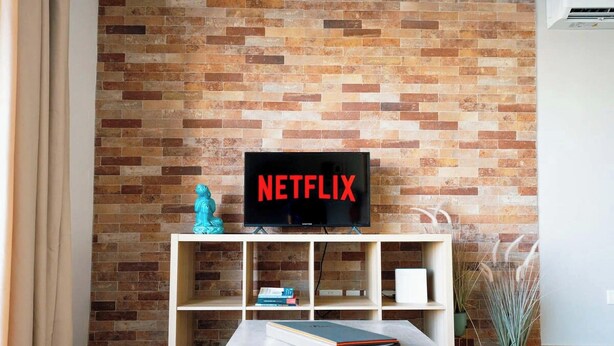 Ett vardagsrum med en tegelvägg, en tv-skärm som visar "NETFLIX", en liten Buddha-staty och en bokhylla.