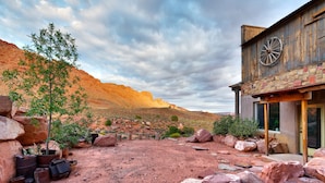 Un bâtiment rustique doté d’une grande fenêtre circulaire, entouré d’un paysage rocheux et d’une végétation clairsemée.