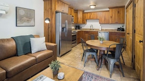 Une cuisine compacte avec des meubles en bois, un réfrigérateur en acier inoxydable, une table à manger avec des chaises et un canapé en cuir marron.