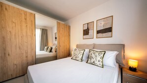 Habitación de hotel con una cama grande, armario de madera, dos cuadros en la pared y una lámpara de noche.