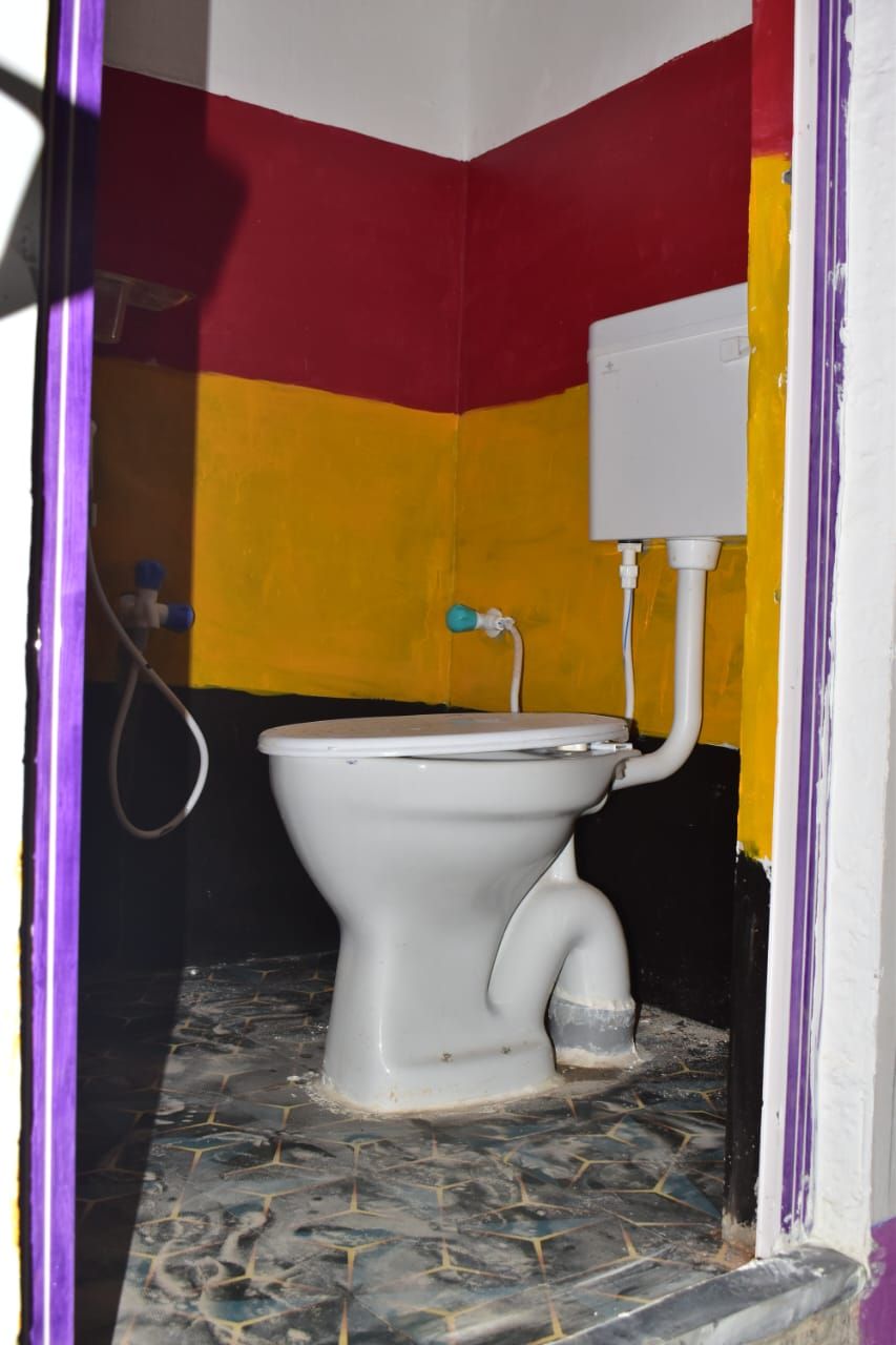 A bathroom with a toilet, a visible pipe, and a wall with a yellow and red color scheme.