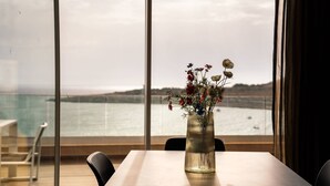 Une table ornée d’un vase de fleurs, avec une vue sur la mer par de grandes fenêtres.