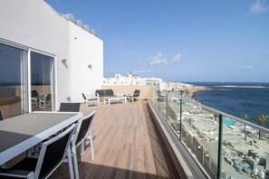Ein Balkon mit Tisch und Stühlen, der Blick auf einen Strand und das Meer freigibt.
