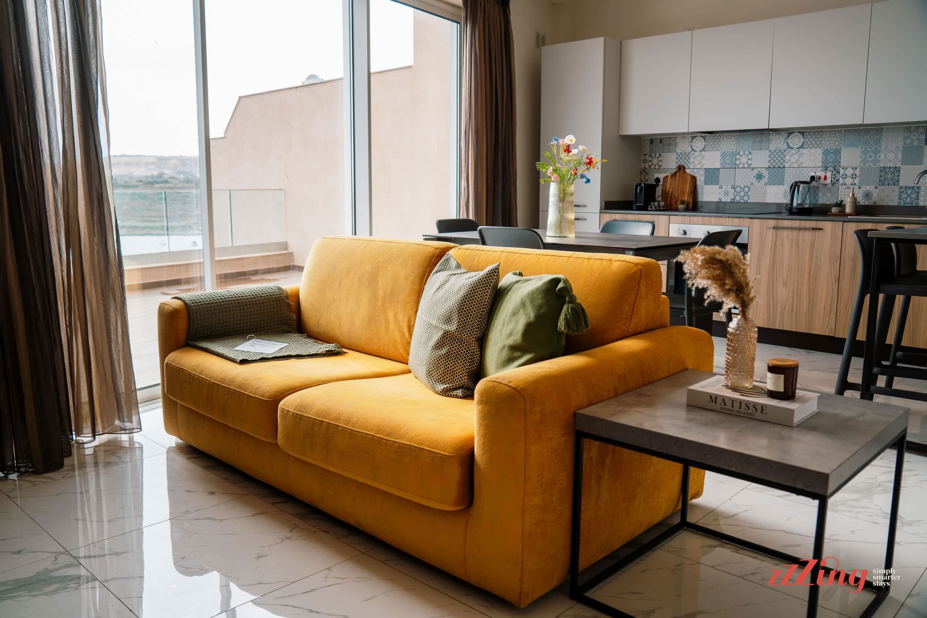 Een moderne woonkamer met een geel sofa, een bijzettafeltje en uitzicht op de keuken.