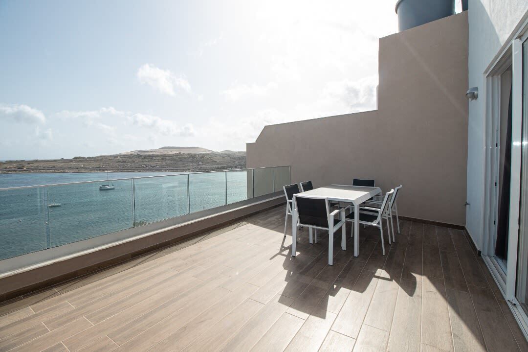 Ein Balkon mit Tisch und Stühlen mit Blick auf ein Gewässer und Land in der Ferne.