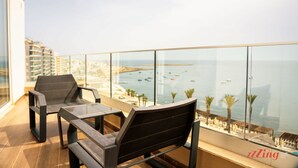 Un balcon avec deux chaises et une table, donnant sur une zone côtière avec des bâtiments et des bateaux.