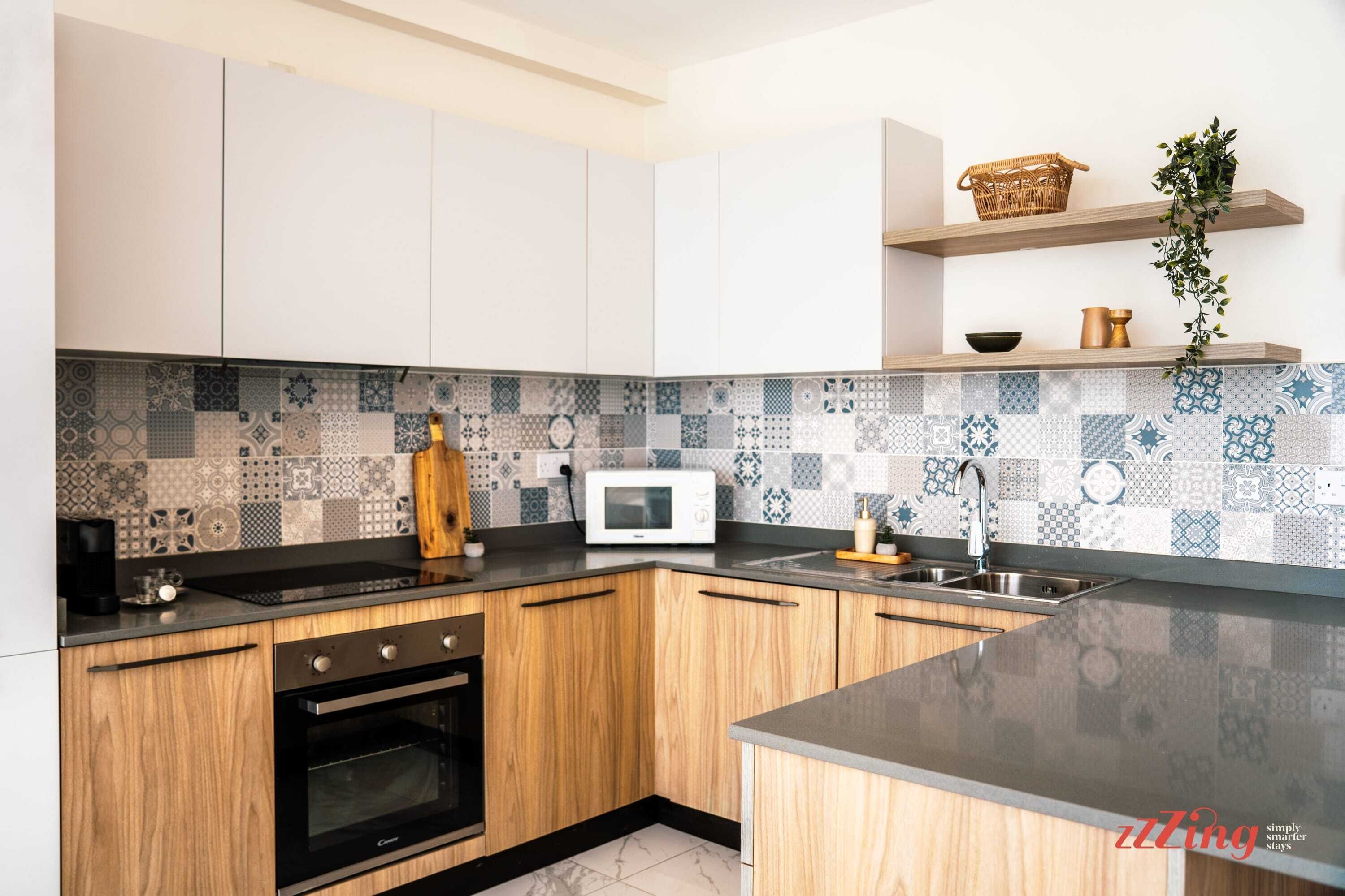 A modern kitchen with white cabinets, a black countertop, and a patterned backsplash.