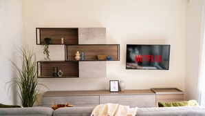 Un salon moderne avec un téléviseur fixé au mur qui affiche le logo « NETFLIX », un canapé gris, une table basse et une plante.