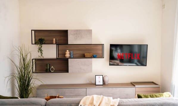 A modern living room with a mounted TV displaying 'NETFLIX', a grey sofa, a coffee table, and a plant.