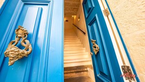 Une porte bleue ornée de magnifiques poignées dorées, qui donne sur un escalier aux marches blanches et un mur de couleur beige.