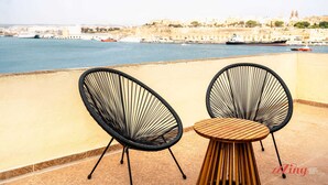 Dos sillas de estructura metálica negra y una mesa de madera en un balcón con vista a la ciudad.