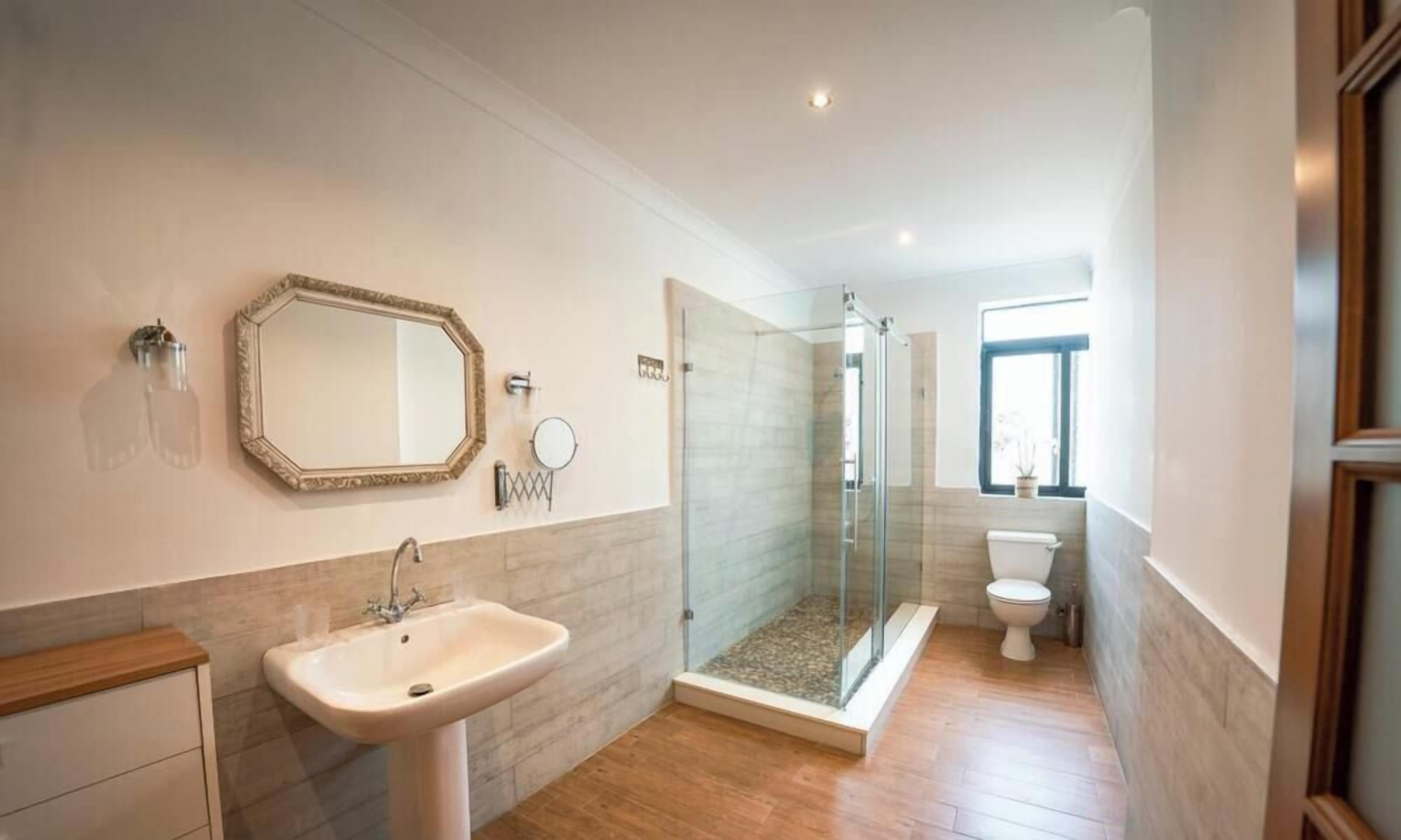 A modern bathroom with a large mirror, a sink, a glass-enclosed shower, and a toilet.