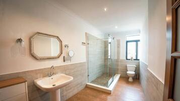 A modern bathroom with a large mirror, a sink, a glass-enclosed shower, and a toilet.