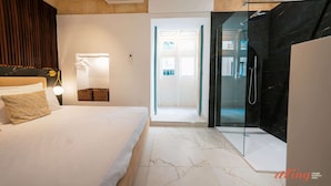 Una habitación de hotel moderna con cama, lámpara de noche y zona de ducha con vidrio.