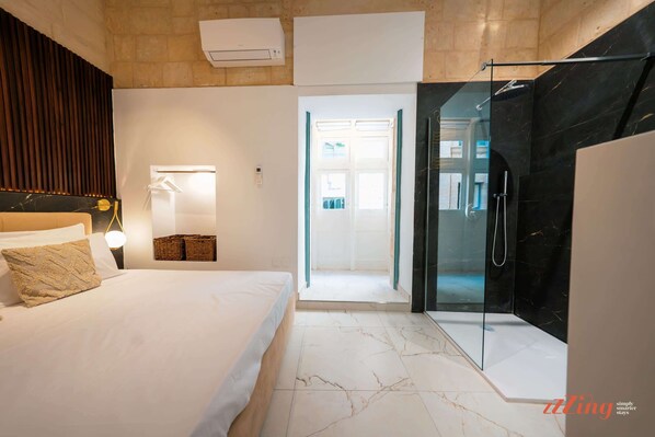 A modern hotel room with a bed, bedside lamp, and a glass-enclosed shower area.