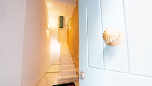 Una escalera que lleva a una puerta con pomo texturizado, un interruptor de luz y un felpudo que dice 'amazing'.