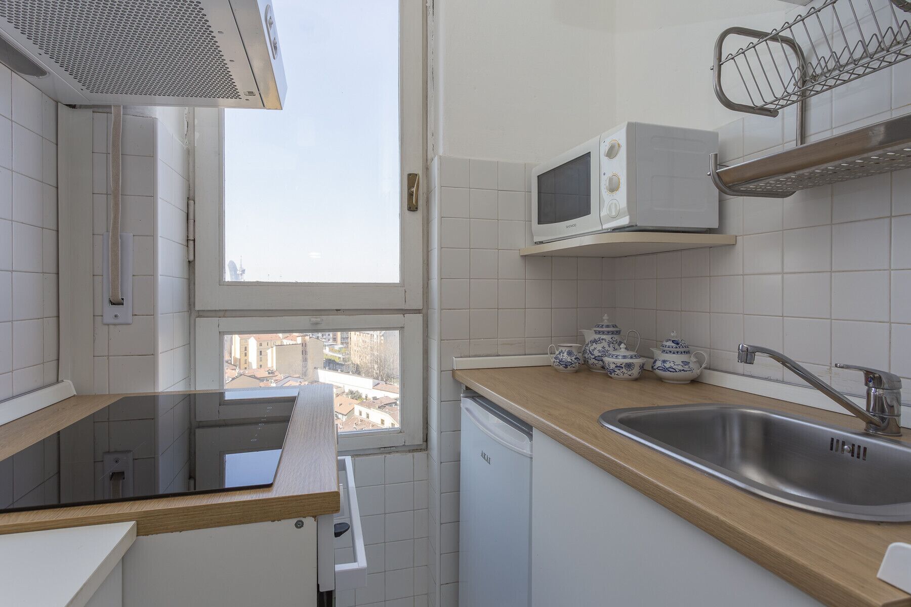 A compact kitchen with a built-in microwave, a stainless steel sink, and a window overlooking a cityscape.