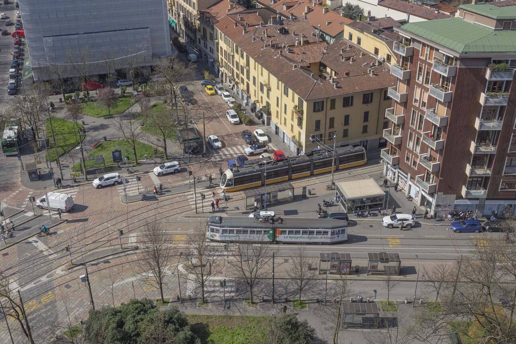 Een tramhalte met een tram, auto's en voetgangers.