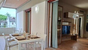 Comedor con mesa preparada para cuatro, televisor y puerta corrediza que da a otra habitación.