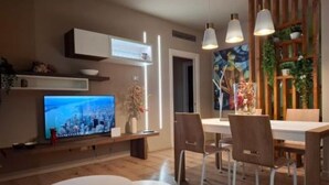 Una sala moderna con televisor de pantalla plana, una mesa de comedor con sillas e iluminación colgante.