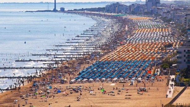 Una playa con hileras de sombrillas y gente.