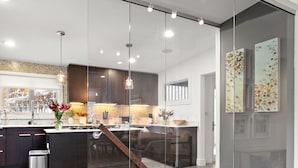 A modern kitchen with a glass partition, a wooden staircase, and a view into the dining area.