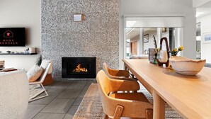 A modern living room with a stone wall, a fireplace, a dining area, and a television displaying "ROXY RENTALS".