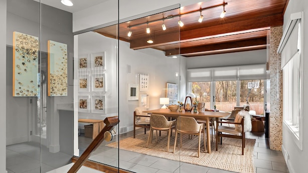 A modern dining area with a wooden table and chairs, a glass partition, and a view of the outdoors.