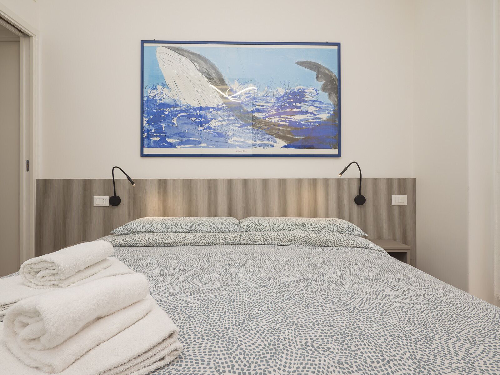 Ein Hotelzimmer mit einem Bett, einem an der Wand befestigten Kunstwerk von einem Wal und einem ordentlich gefalteten Stapel Handtücher.
