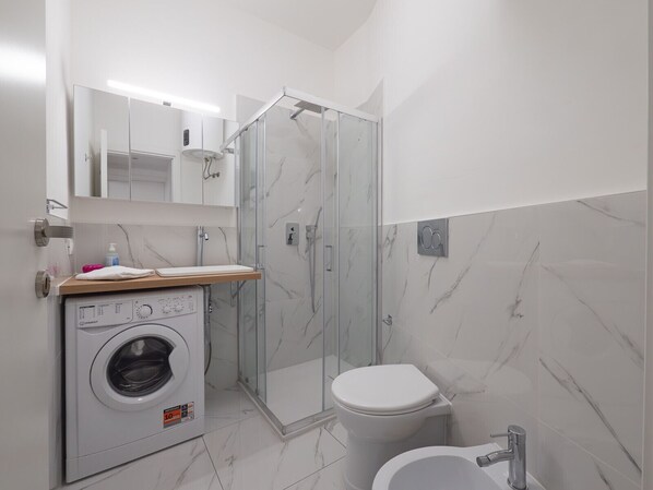 A modern bathroom with a glass-enclosed shower, a built-in washing machine, and a toilet.