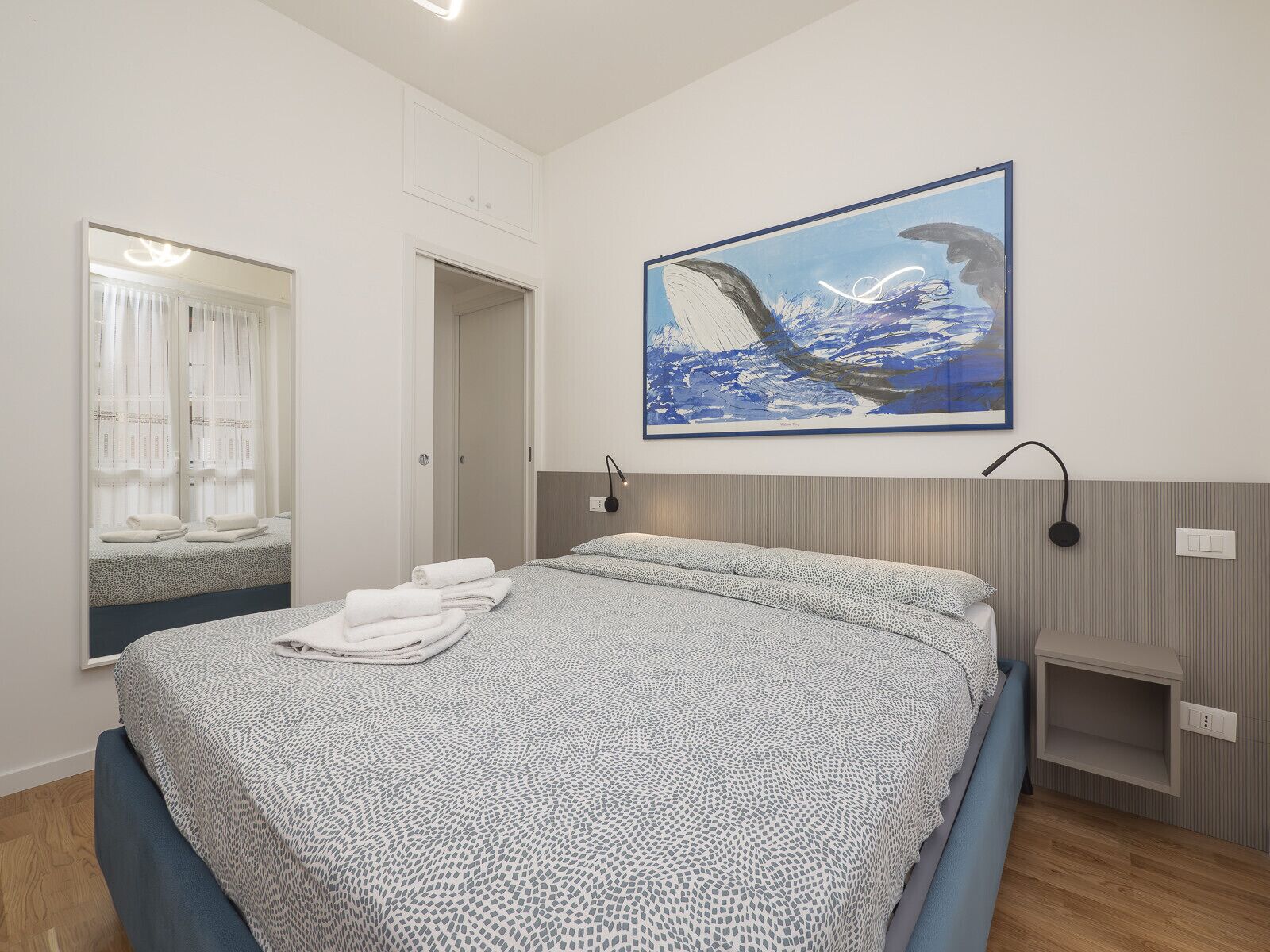 Ein modernes Schlafzimmer mit einem Bett, einem großen Spiegel, einem Gemälde und einem Nachttisch.