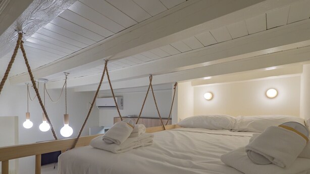Une chambre à coucher avec un lit, du linge de lit blanc et des ampoules suspendues.