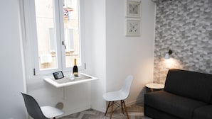 Un salon moderne avec un canapé gris, une petite table blanche sur laquelle se trouvent une bouteille et une tablette, deux chaises blanches et un parquet à motifs chevrons.