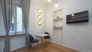 Une chambre moderne avec un plancher en bois, une table avec des chaises, un téléviseur fixé au mur et une étagère ornée d’objets décoratifs.