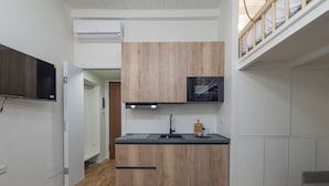 Une cuisine de taille réduite avec des meubles en bois, un plan de travail noir et un four à micro-ondes encastré.