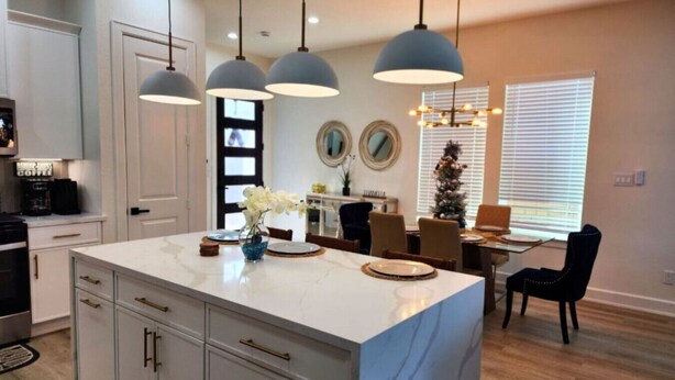 A modern kitchen with a marble island, pendant lights, and a dining area with a Christmas tree.