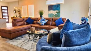 A living room with a brown leather sectional sofa, a glass coffee table, and a blue armchair.