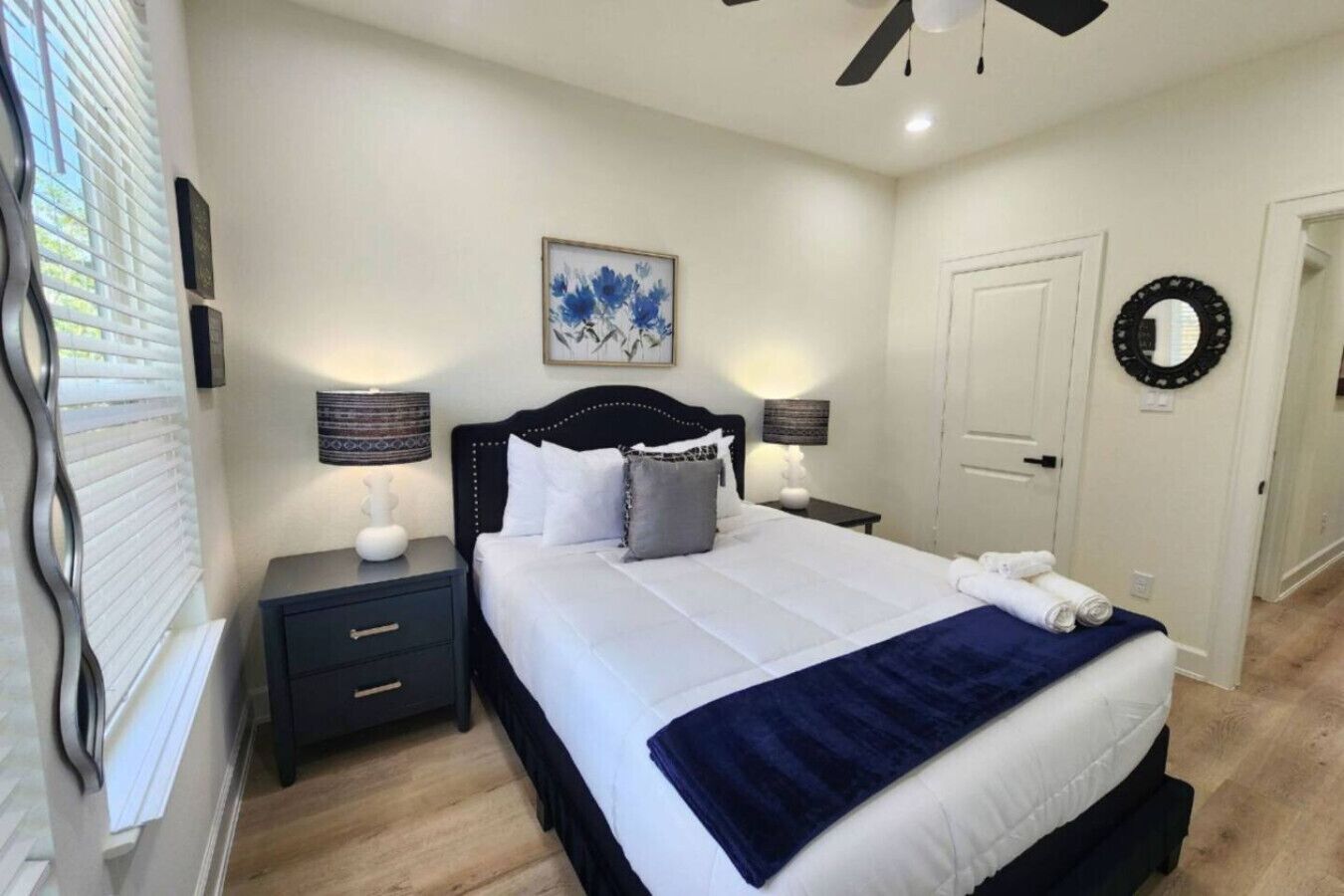 A neatly arranged bedroom with a bed, bedside tables, a ceiling fan, and a door.