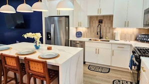 A modern kitchen with white cabinets, stainless steel appliances, and pendant lighting.