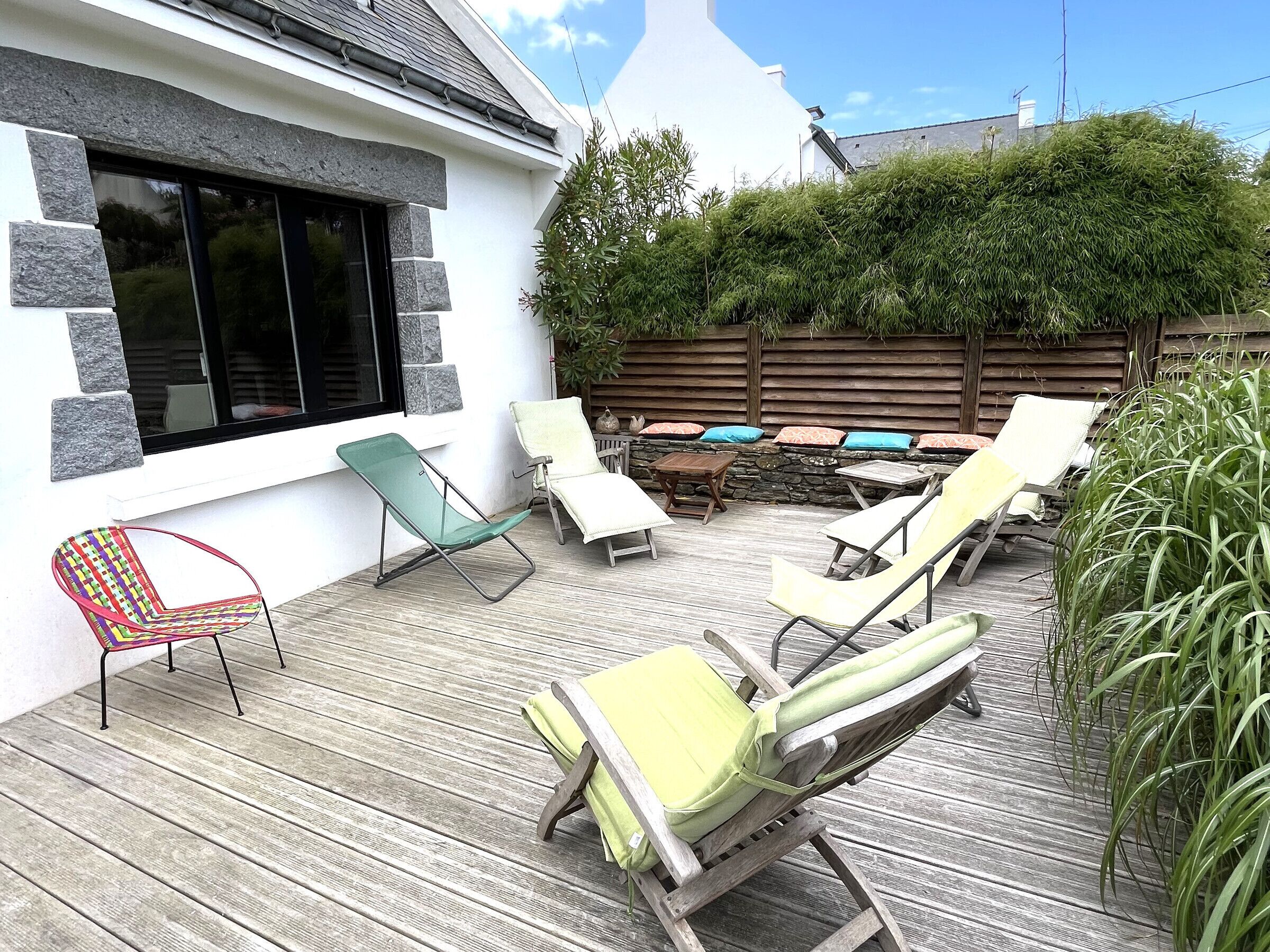 A patio with outdoor furniture, including a variety of chairs and a table, set against a white wall with stone accents.