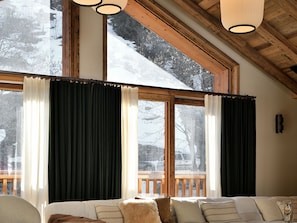 A cozy room with a large window, wooden ceiling beams, and a view of a snowy landscape.