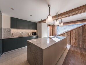 A modern kitchen with dark cabinets, a marble countertop, and pendant lighting. - Luxury 4-bedroom apartment with 5* concierge, mountain view (Les Allues)